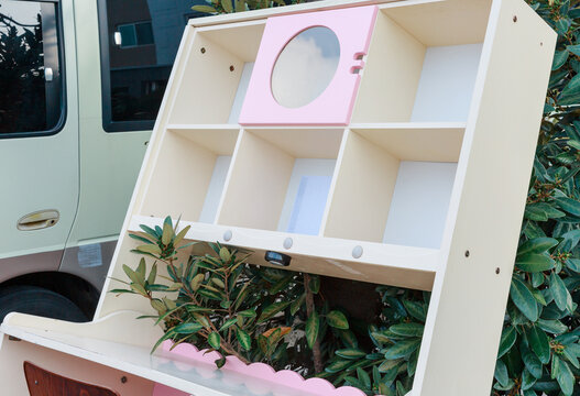 Abandoned pink bookshelf next to a tree.
