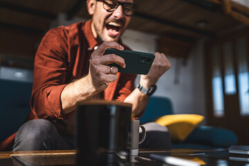 caucasian man sit at home play video games on smartphone mobile phone