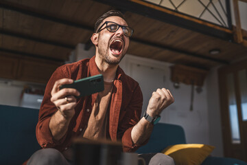 caucasian man sit at home play video games on smartphone mobile phone