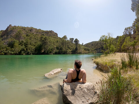 Woman relaxing on rock in natural pond shore in beautiful scenery. UG 