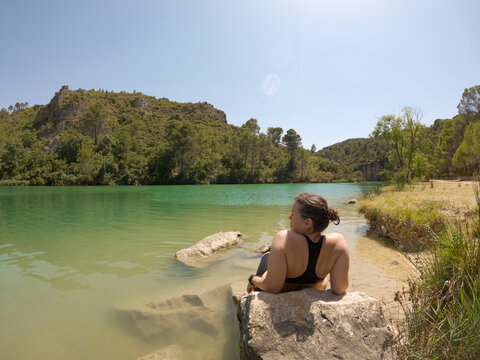 Woman relaxing on rock in natural pond shore in beautiful scenery. UG 
