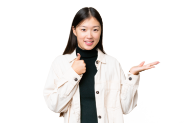 Young Asian woman over isolated chroma key background holding copyspace imaginary on the palm to insert an ad and with thumbs up