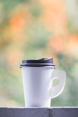 A paper cup of coffee or tea put on the edge with blurred nature background.