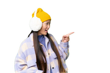 Young Asian woman wearing winter muffs over isolated chroma key background pointing finger to the side and presenting a product