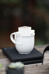 Dripping coffee with white coffee bag in white cup on wood table.