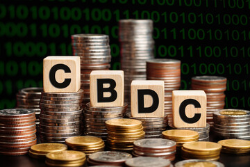 The word CBDC (Central Bank Digital Currency) on wooden cube with stacks of coins. Central Bank...