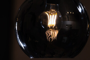 Round glass lampshade with a tungsten lamp inside glowing in the dark
