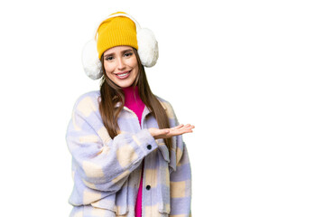 Young woman wearing winter muffs over isolated chroma key background presenting an idea while looking smiling towards