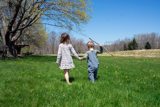 Siblings Walk Together Holding Hands on Green Grass in Spring