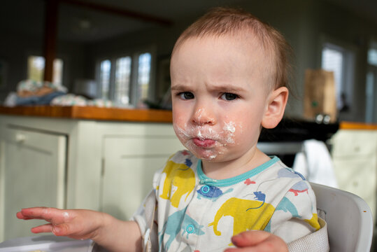 Toddler with Messy Face Sits in High Chair in Kitchen at Home