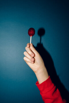 hand holding red lollipop agains blue background 
