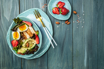 Healthy nutritious paleo keto breakfast diet two eggs, avocado, grilled chicken fillet, nuts, strawberries and fresh salad. Keto breakfast or lunch. place for text, top view
