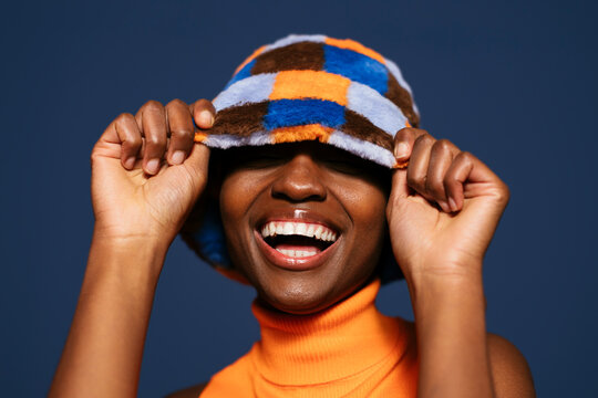 Happy woman hiding eyes with hat against blue background