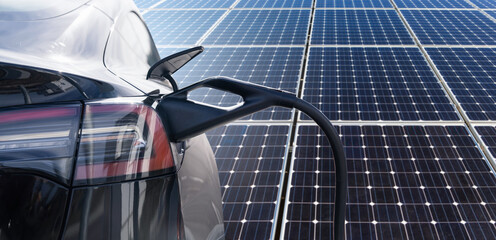 Close up of electric car with a connected charging cable on the background of solar panels