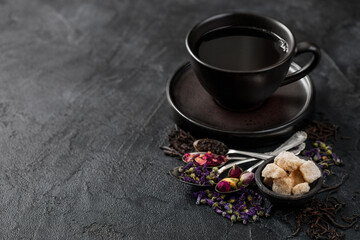 Obraz na płótnie Canvas Tea cup with spoons and various tea on black background. Black and green loose tea,rose buds,blue mallow flowers
