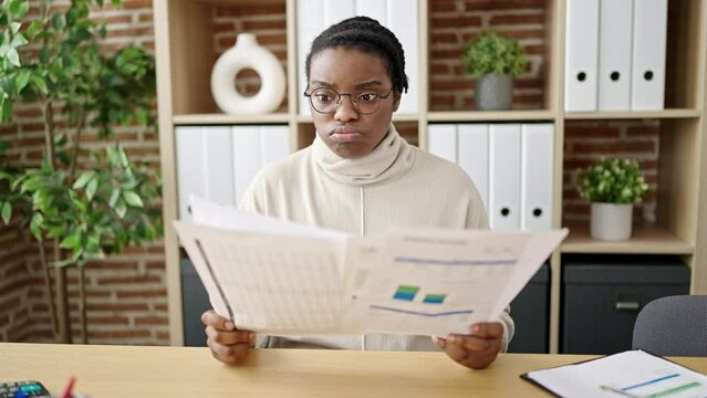 African american woman business worker reading document with worried expression holding dollars to be happy at office