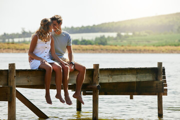 Couple sitting on jetty, relax by lake and summer, travel and adventure, love and care outdoor. People in relationship, trust and bonding on vacation, man and woman with freedom and forehead touch
