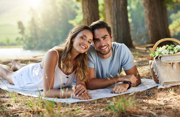 Couple on picnic, portrait and relax together in nature park, happy people with travel and bonding outdoor. Happiness, man and woman lying down and commitment with trust and love in relationship