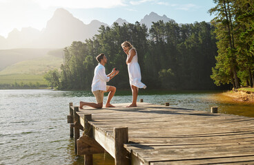 Man, woman and engagement proposal by lake on vacation with surprise, wow or happiness in sunshine. Couple, marriage offer and ring in nature for romance, love and happy on holiday in summer by water - Powered by Adobe