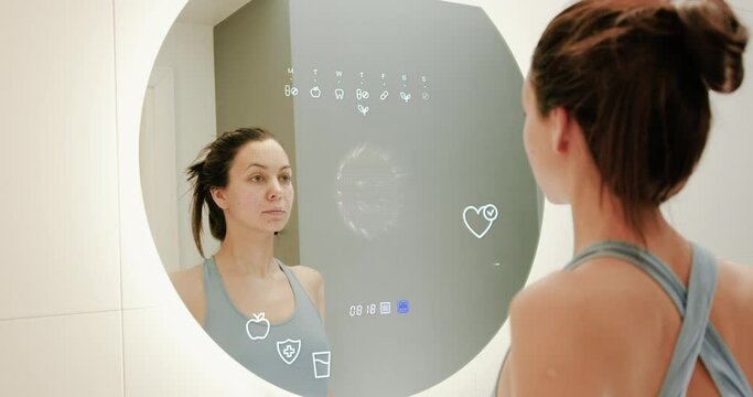 Woman in smart home looking to smart mirror screen and do morning work-out during this procedure mirror makes face scan and health measures