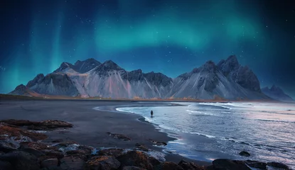 Fotobehang Nachtblauw Incredible Iceland nature seascape. Iconic location for landscape photographers and bloggers. Scenic Image of Iceland. Alone tourist against Vestrahorn mountaine with Green northern lights  © jenyateua