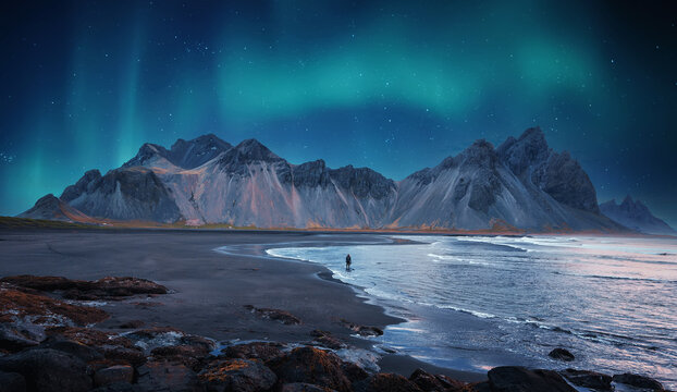 Incredible Iceland nature seascape. Iconic location for landscape photographers and bloggers. Scenic Image of Iceland. Alone tourist against Vestrahorn mountaine with Green northern lights