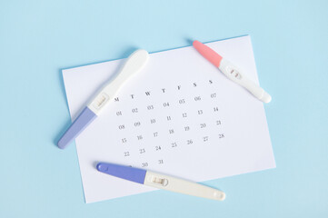 Top view of an inkjet pregnancy test with a biochemical reaction between hCG and urine appearing in two bars above a white calendar with last menstrual dates marked. Ovulation day. Planning maternity