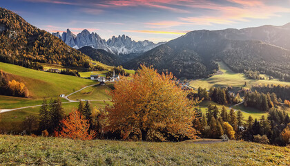 Incredible nature landscape in the Dolomites mountains. Fantastic autumn View on mountain valley, alone colorful tree under sunlight. Famous view in Santa Maddalena village during sunset