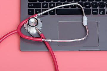 Medyczny stetoskop leży na różowym tle i klawiaturze laptopa, ciąża