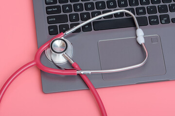 Czerwony stetoskop leżący na klawiaturze komputera na różowym tle - obrazy, fototapety, plakaty