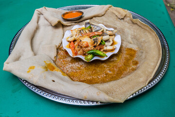 Meal in Ethiopia - pieces of fish with chilli peppers and vegetables on injera flat bread