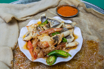 Meal in Ethiopia - pieces of fish with chilli peppers and vegetables on injera flat bread