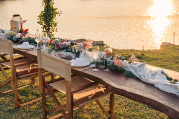 Fototapeta na wymiar Rustic style dining table with flower, wine glass, candle decoration at dinner by the river in the sunset