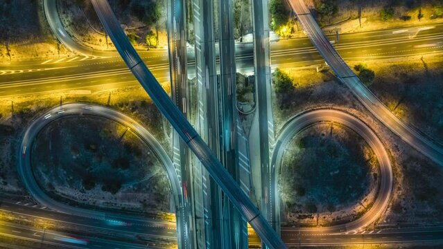 Elevated top view time-lapse of car traffic at multiple lane highway. Aerial view zoom out of highway road intersection and city traffic at night. Urban cityscape concept, Spain