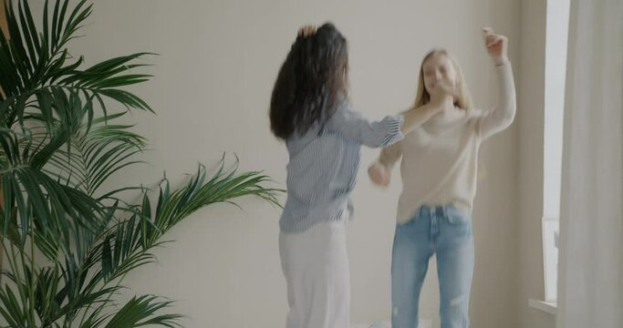 Young women sisters in casual clothes jumping on bed laughing dancing to music in bedroom at home. Friendship and positive emotion concept.
