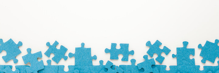 Different many blue puzzle pieces on white table background. Closeup. Top down view. Wide banner. Empty place for text.