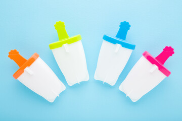 White plastic containers for homemade ice popsicle on colorful sticks. Light blue table background....