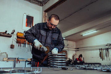 Locksmith in special clothes and goggles works in production. Metal processing with angle grinder. Sparks in metalworking.