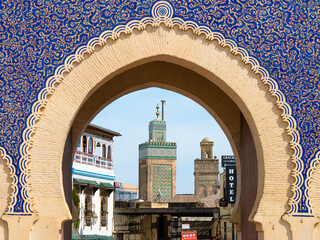 Minaret of the Bou Inania Madrasa seen through the iconic Bab Bou Jeloud in Fez, Morocco on a sunny...