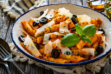 Noodles with pesto, parmesan cheese, basil and black olives served on wooden table
