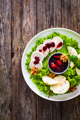 Fresh salad - goat cheese, pear, jam, lettuce and walnuts on wooden background
