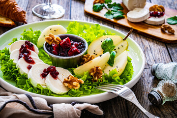 Fresh salad - goat cheese, pear, jam, lettuce and walnuts on wooden background

