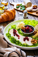 Fresh salad - goat cheese, pear, jam, lettuce and walnuts on wooden background
