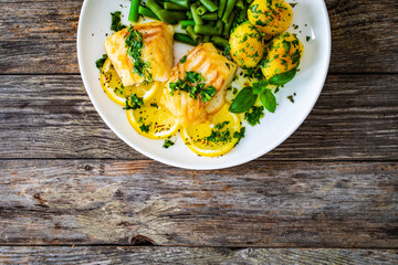 Fish dish - fried cod with baked potatoes and boiled green beans on wooden table