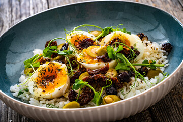 Boiled eggs with boiled white rice, sun dried tomatoes  and green olives on wooden table