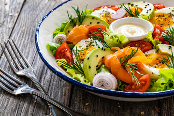 Salmon salad - smoked salmon, hard boiled eggs, avocado and leafy greens on wooden table
