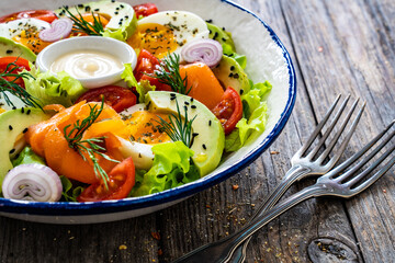 Salmon salad - smoked salmon, hard boiled eggs, avocado and leafy greens on wooden table
