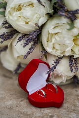 delicate wedding bouquet of large white peonies and lavender and wedding rings in a red case in the shape of a heart