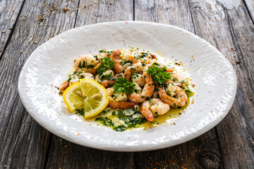 Fried prawns with thyme in cooking pan on wooden table
