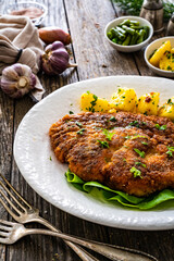 Breaded fried pork chop with green beans and potatoes on wooden table
